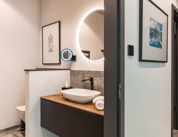 Modernes Badezimmer mit rundem LED-Spiegel und Waschbecken auf einem elegantem Waschtisch im ELBE.6 Apartment I in Wittenberge.