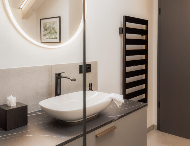 Modernes Bad im ELBE.6 Apartment III mit Designer-Waschtisch, schwarzer Armatur und rundem LED-Spiegel.